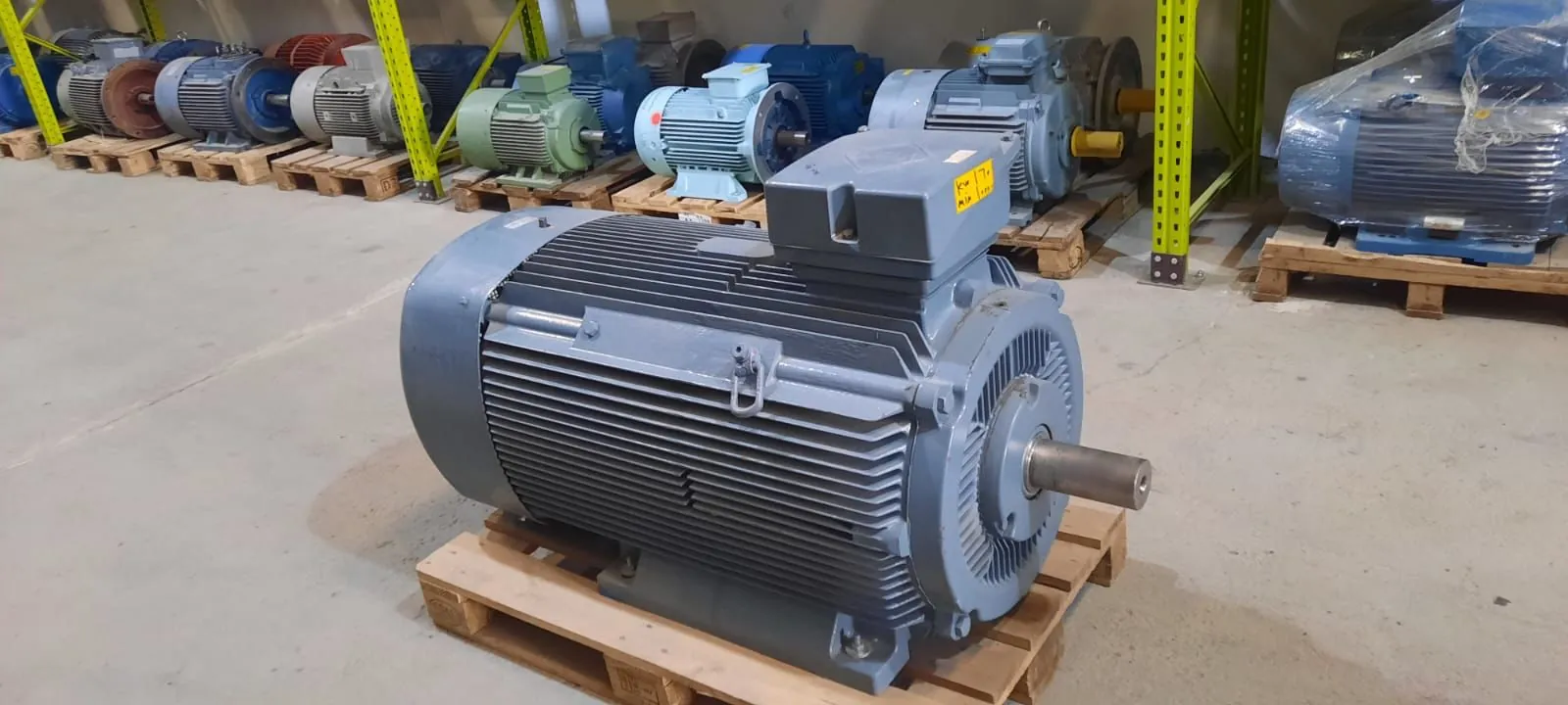 Großer Drehstrom-Elektromotor auf Palette im Lager von Industrietec mit weiteren Industriemotoren im Hintergrund